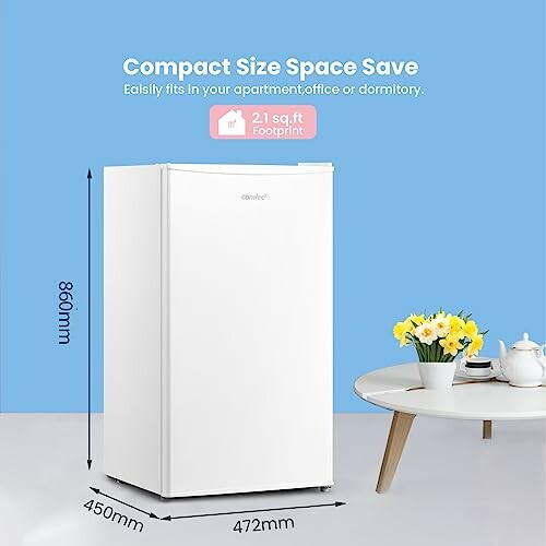 Compact white refrigerator with dimensions, next to a table with flowers.