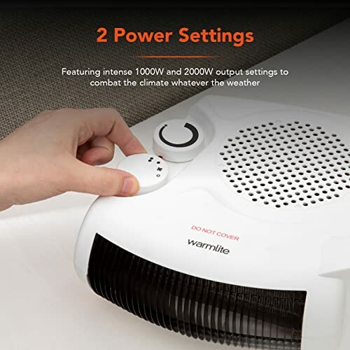 Hand adjusting power setting on white heater with vent and speaker grill.