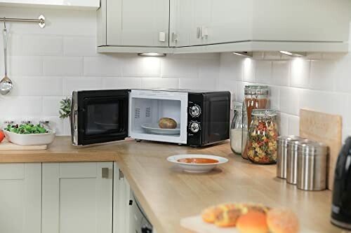 Kitchen counter with open microwave, potato inside, salad, soup, jars, and bread.