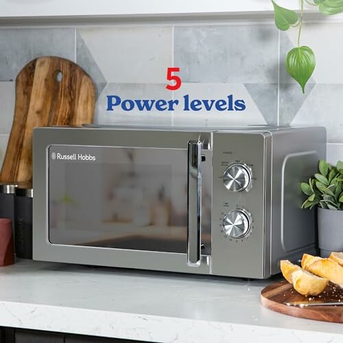 Russell Hobbs microwave on kitchen countertop with bread and herbs, featuring 5 power levels.