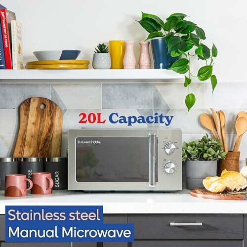 Stainless steel microwave on a kitchen counter with plants and kitchenware.